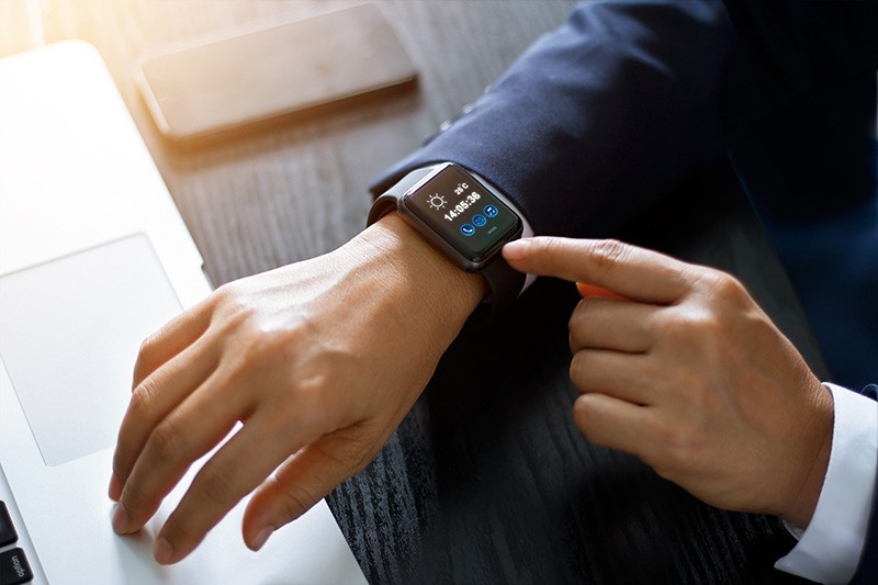 Wearables in business - Businessman using smart watch app over laptop and smartphone on working desk